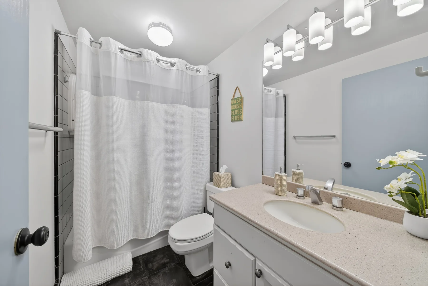 Un baño con cortina de ducha, inodoro y lavabo con mueble.