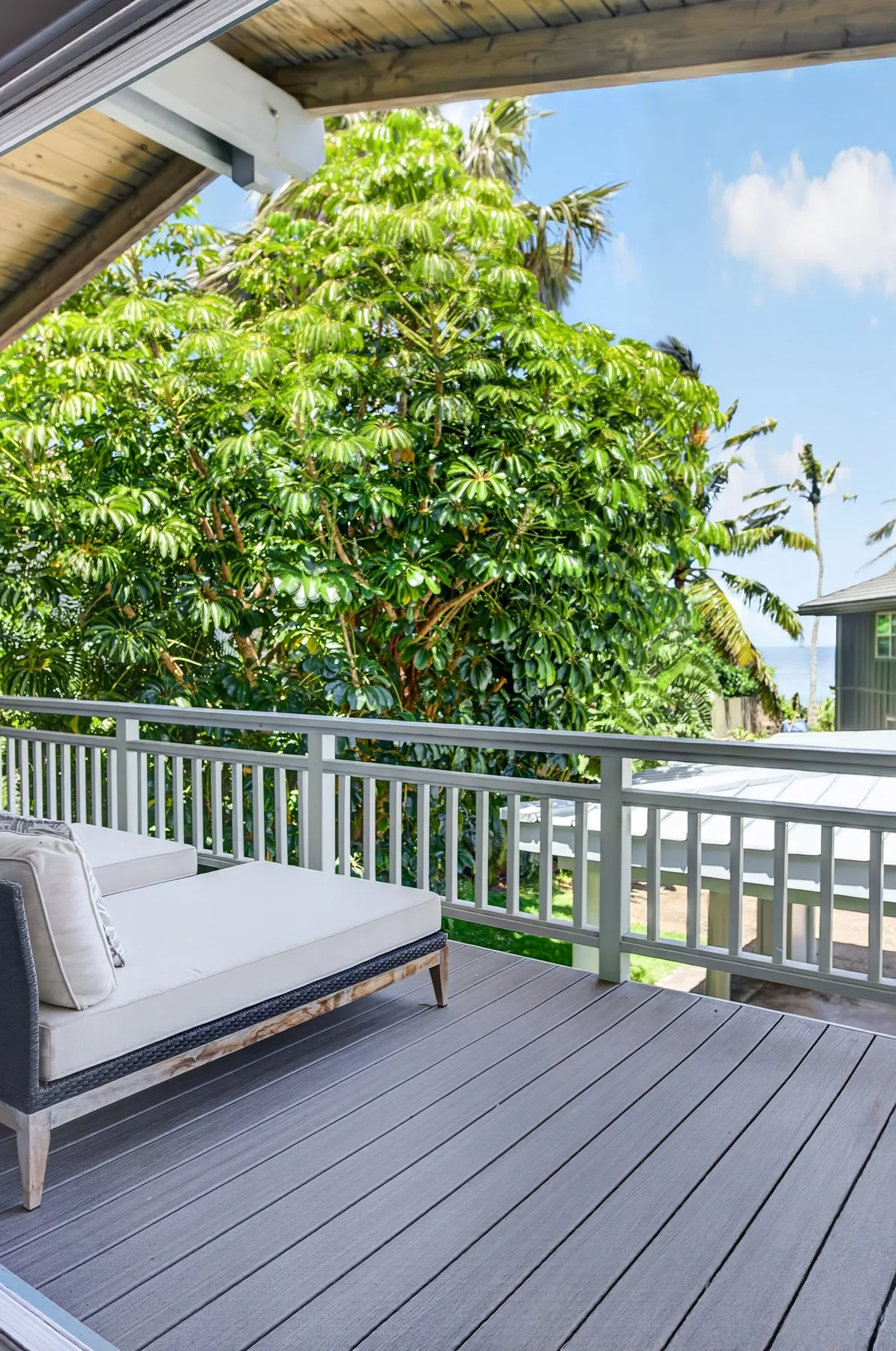 Una terraza exterior con asientos acolchados mira hacia árboles frondosos bajo un techo cubierto.