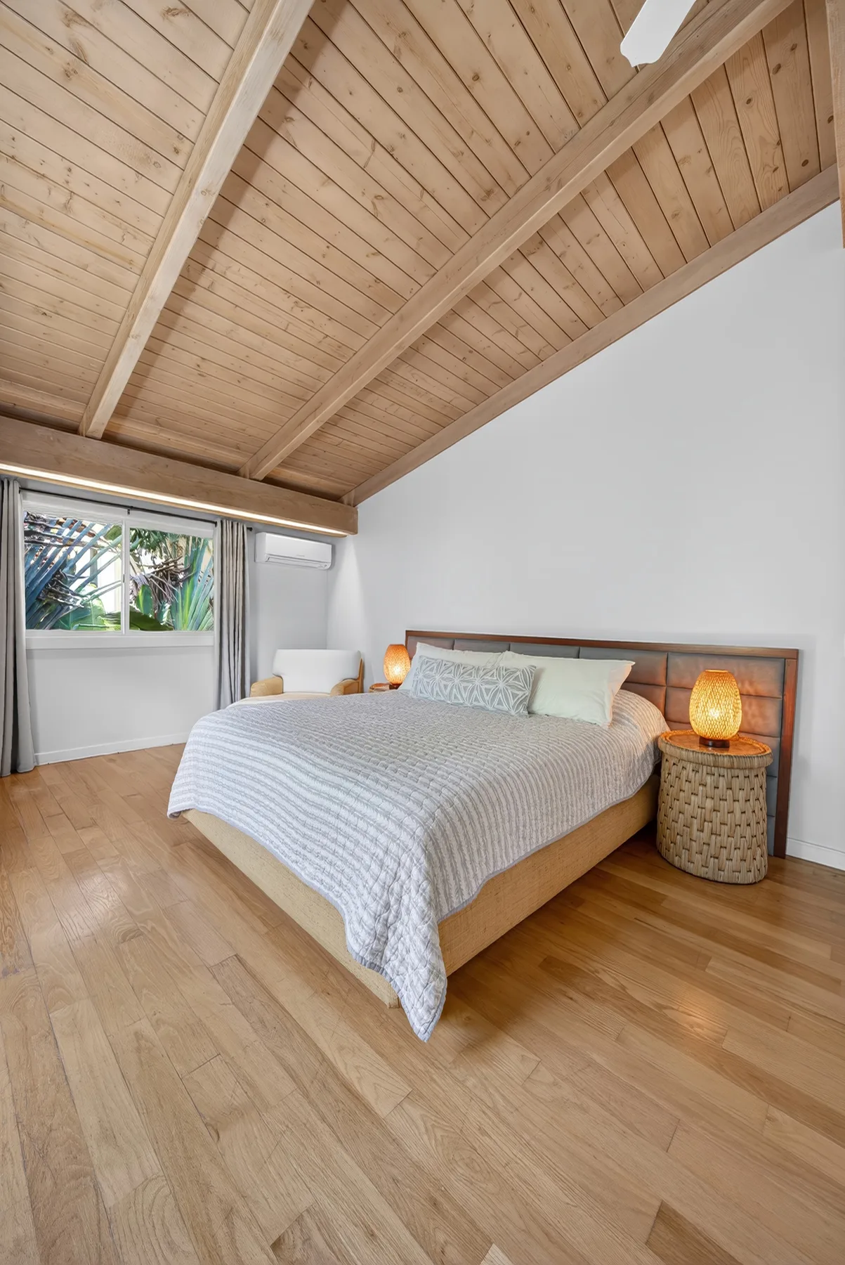 Dormitorio con una cama bajo un techo inclinado de madera y una ventana.
