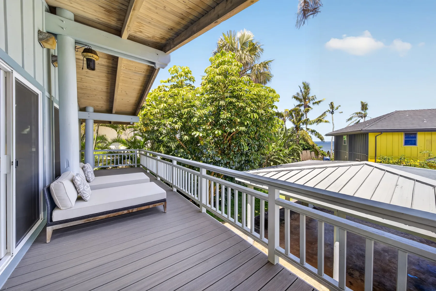 A covered balcony with cushioned seating overlooks trees and neighboring buildings.