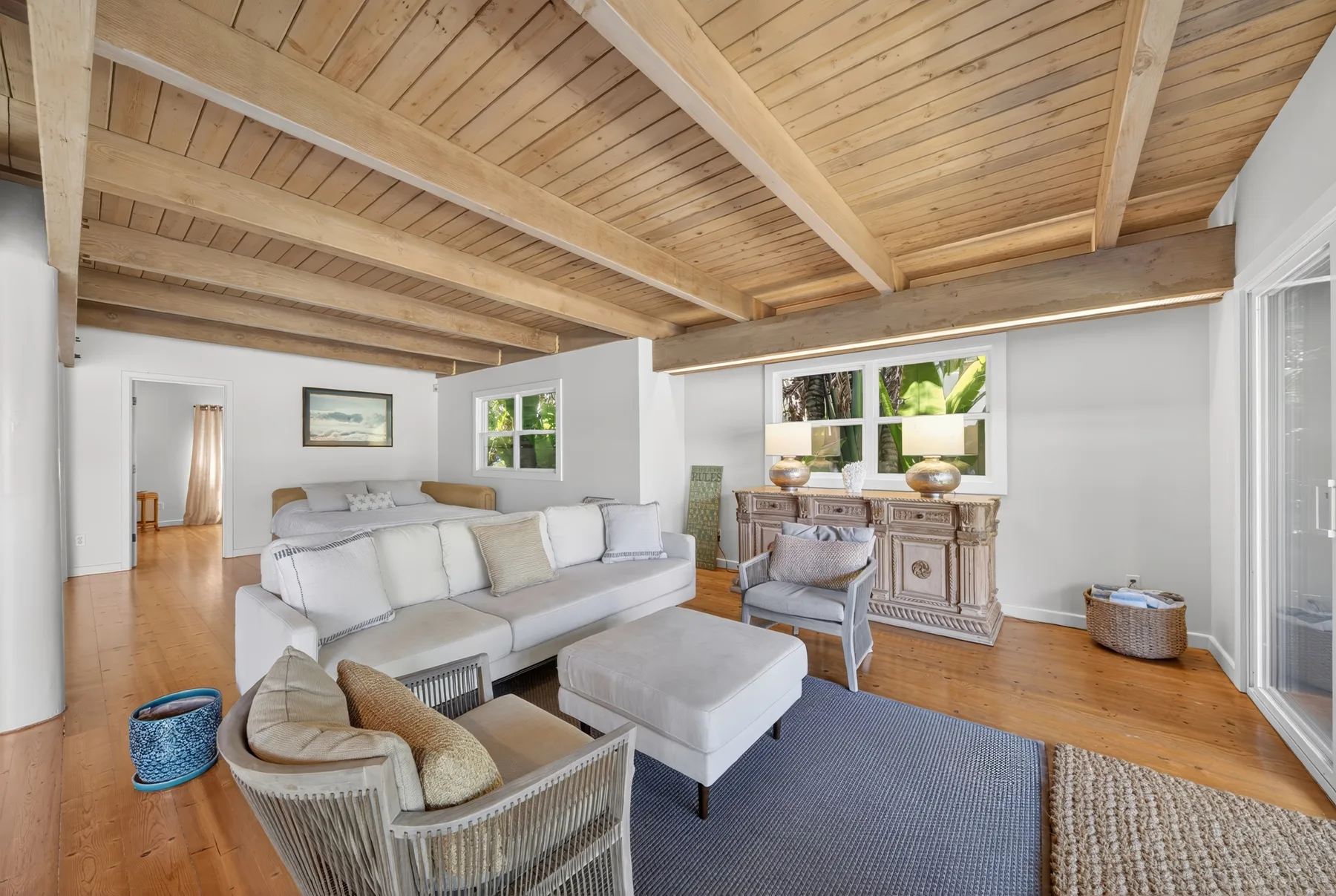 Una sala de estar con asientos bajo un techo alto de madera y grandes ventanas.