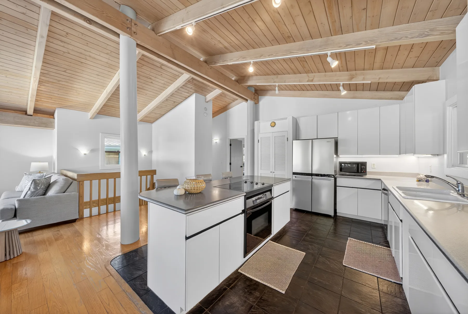 Una cocina abierta con gabinetes blancos y una sala de estar bajo un techo de madera.