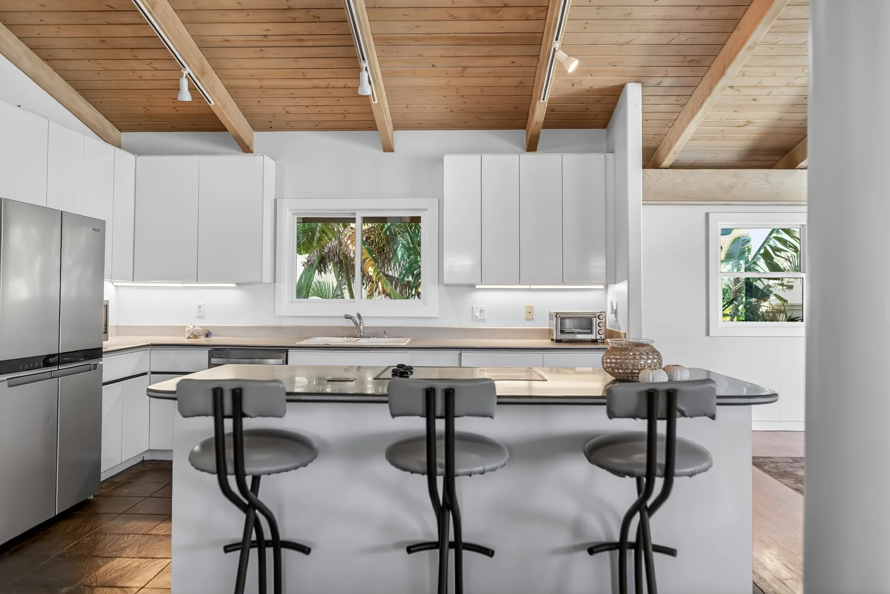 Una cocina luminosa con una isla grande y taburetes bajo un techo de madera.