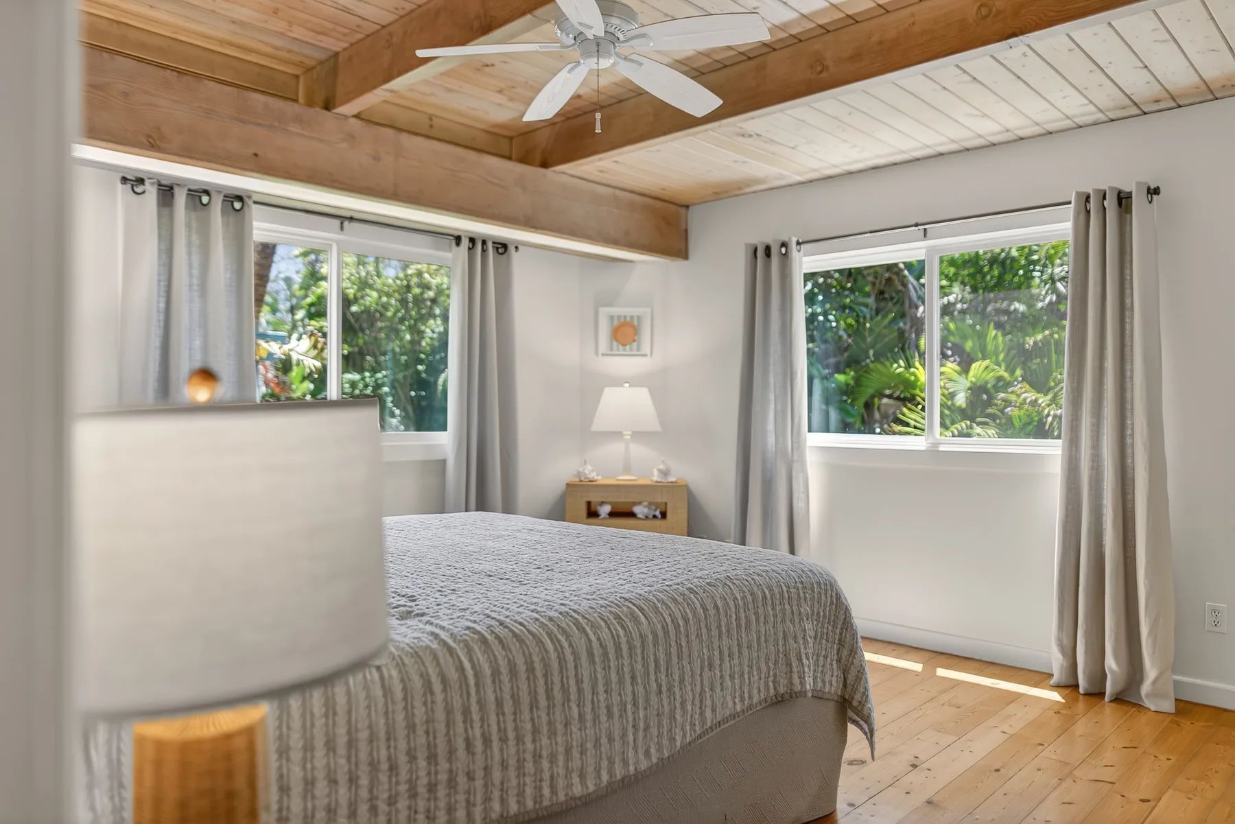 Dormitorio con una cama, ventanas con cortinas y techo revestido de madera.
