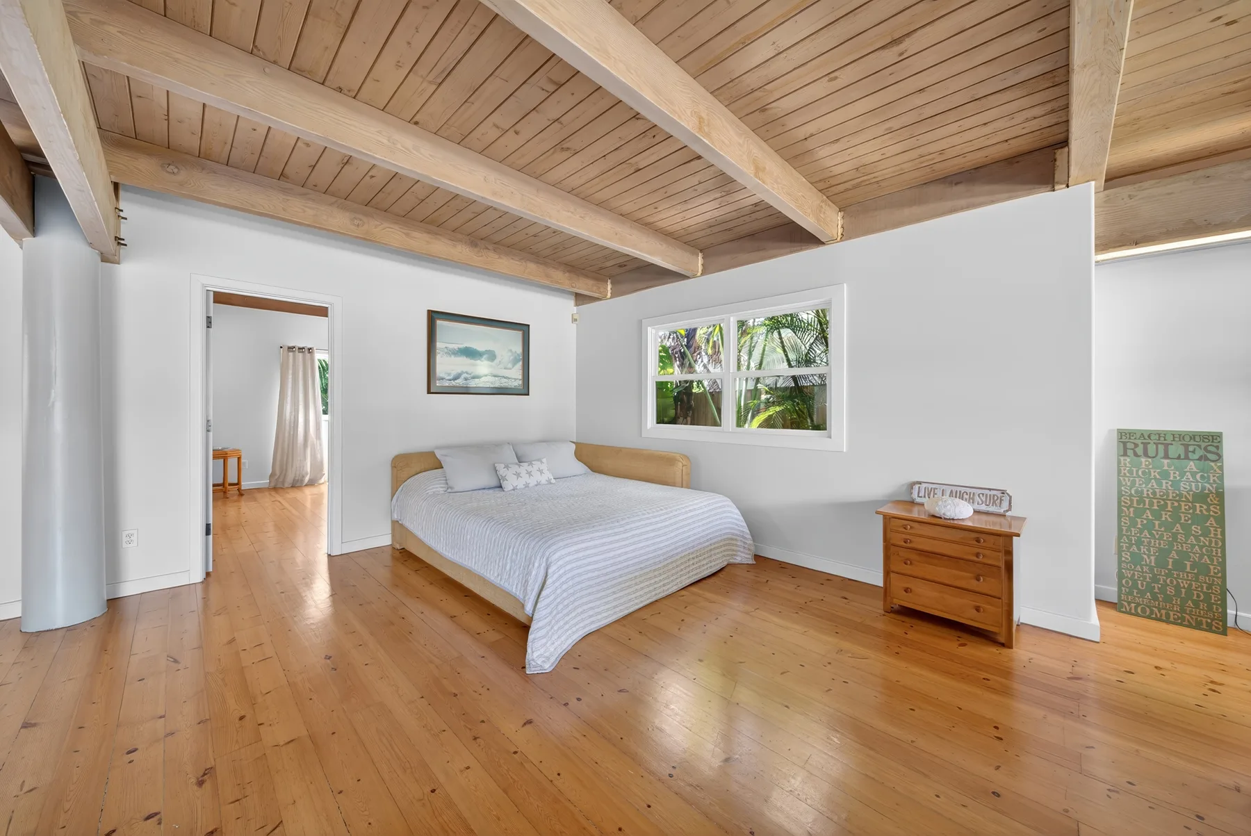 Dormitorio con una cama bajo un techo de madera y ventanas con vistas a la vegetación.