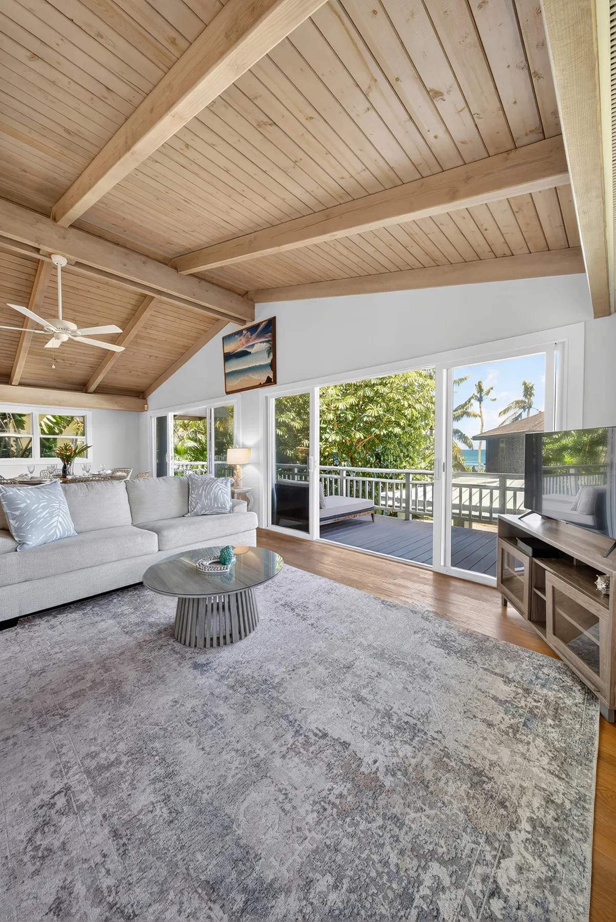 A bright living room with seating, a coffee table, and glass doors opening onto a deck.