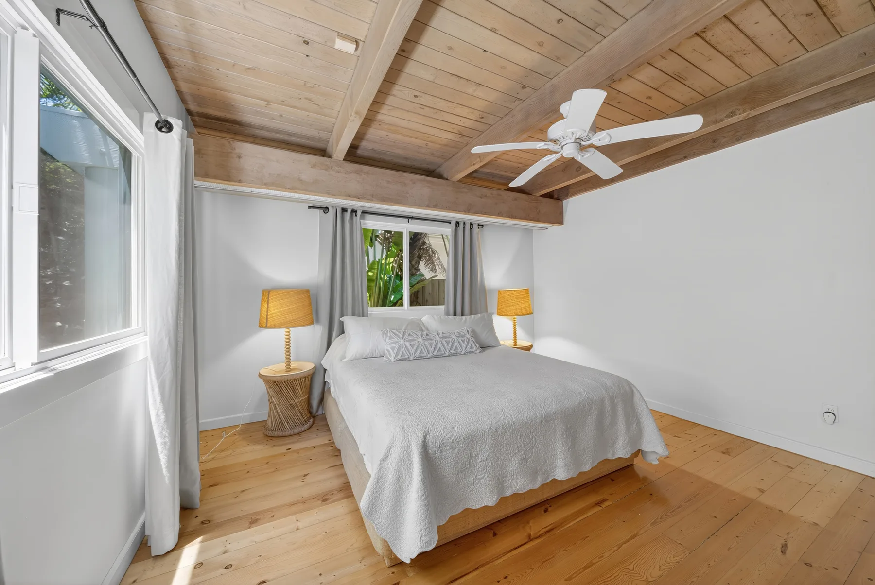 Un dormitorio con una cama bajo un techo de madera inclinado y un ventilador.