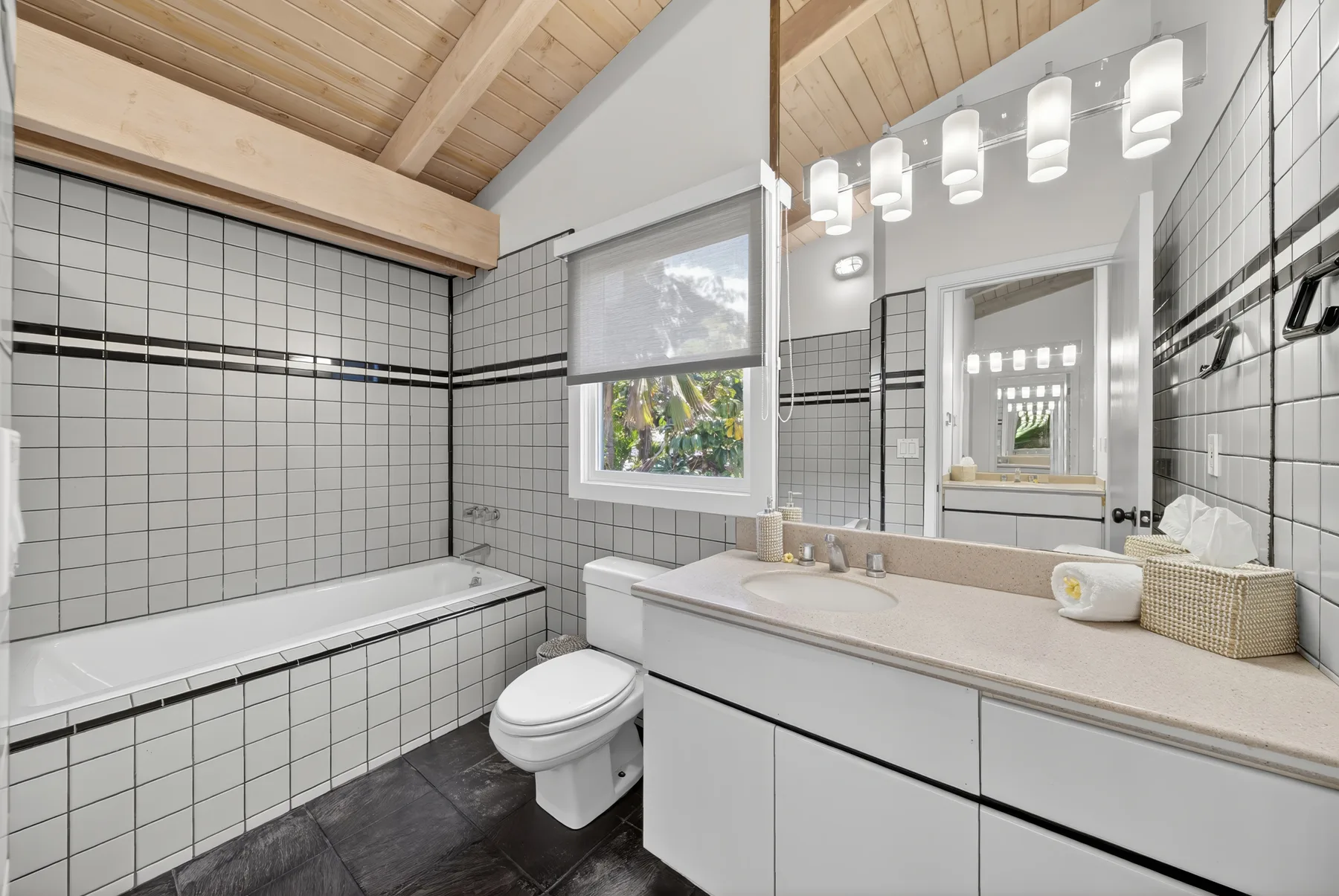 Un baño alicatado con bañera, lavabo y un espejo grande.