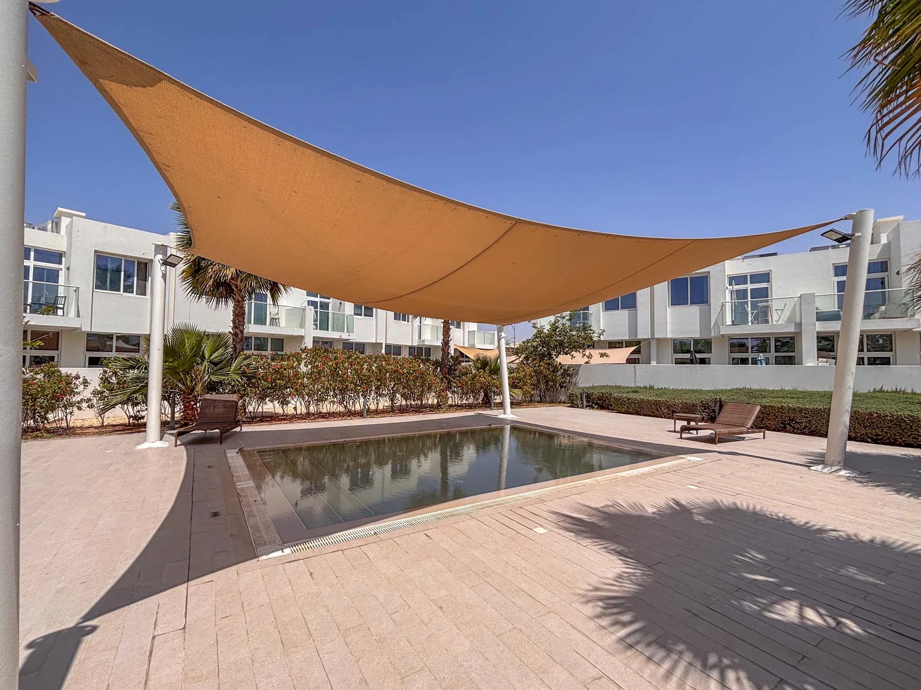 Una piscina rectangular está bajo una gran cubierta de sombra en un patio.