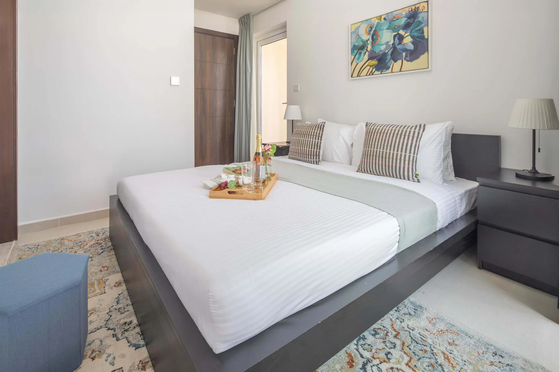 Un dormitorio con una cama bien tendida, cojines estampados y arte colorido encima.
