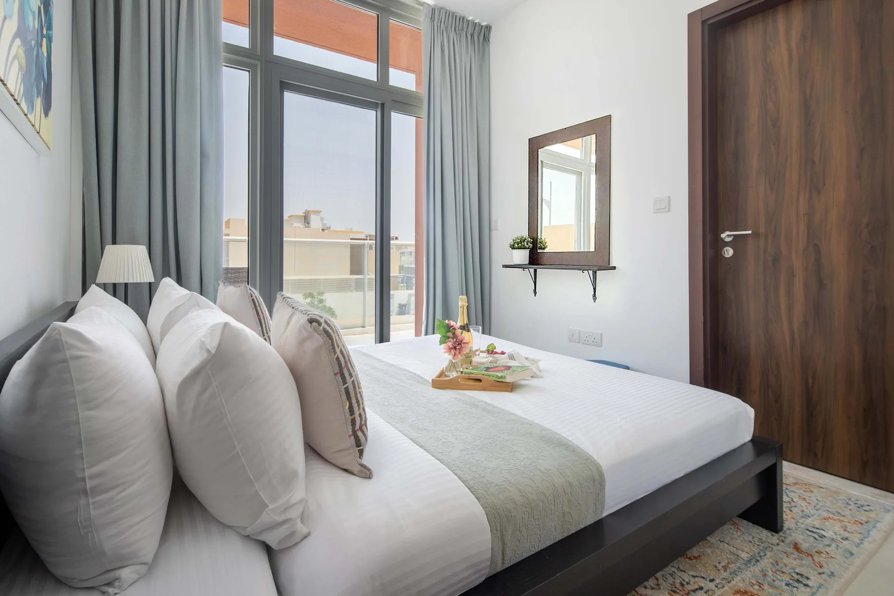 Un dormitorio luminoso con una cama bien hecha junto a una ventana alta con cortinas.