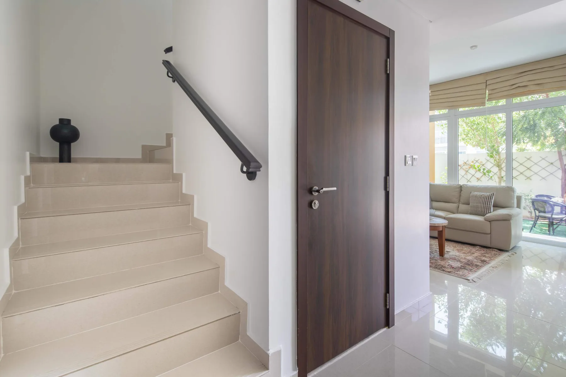 Un pasillo interior con una escalera, una puerta oscura y una zona de estar al fondo.