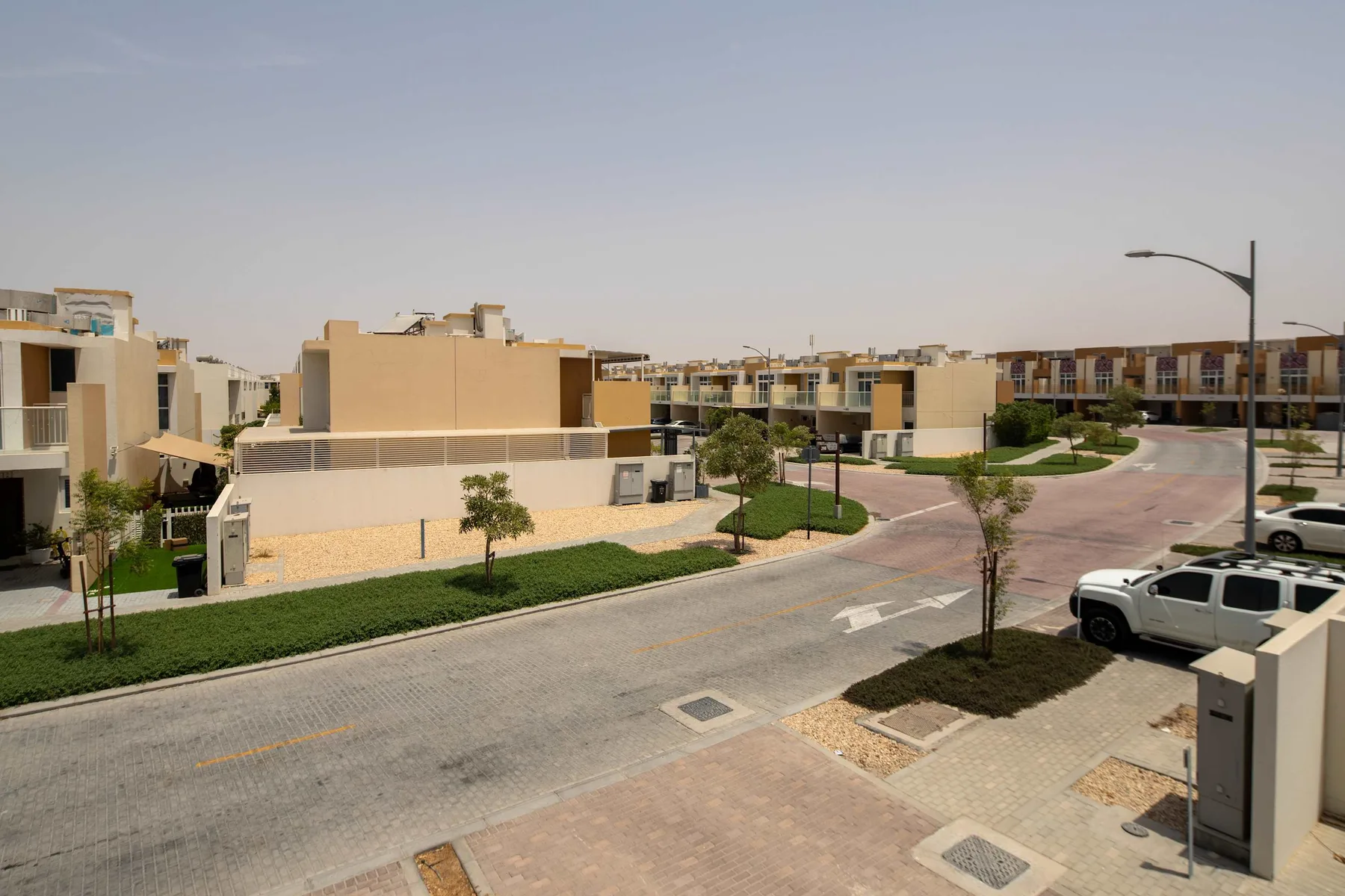 Una calle residencial curva junto a viviendas modernas, jardines y vehículos estacionados.