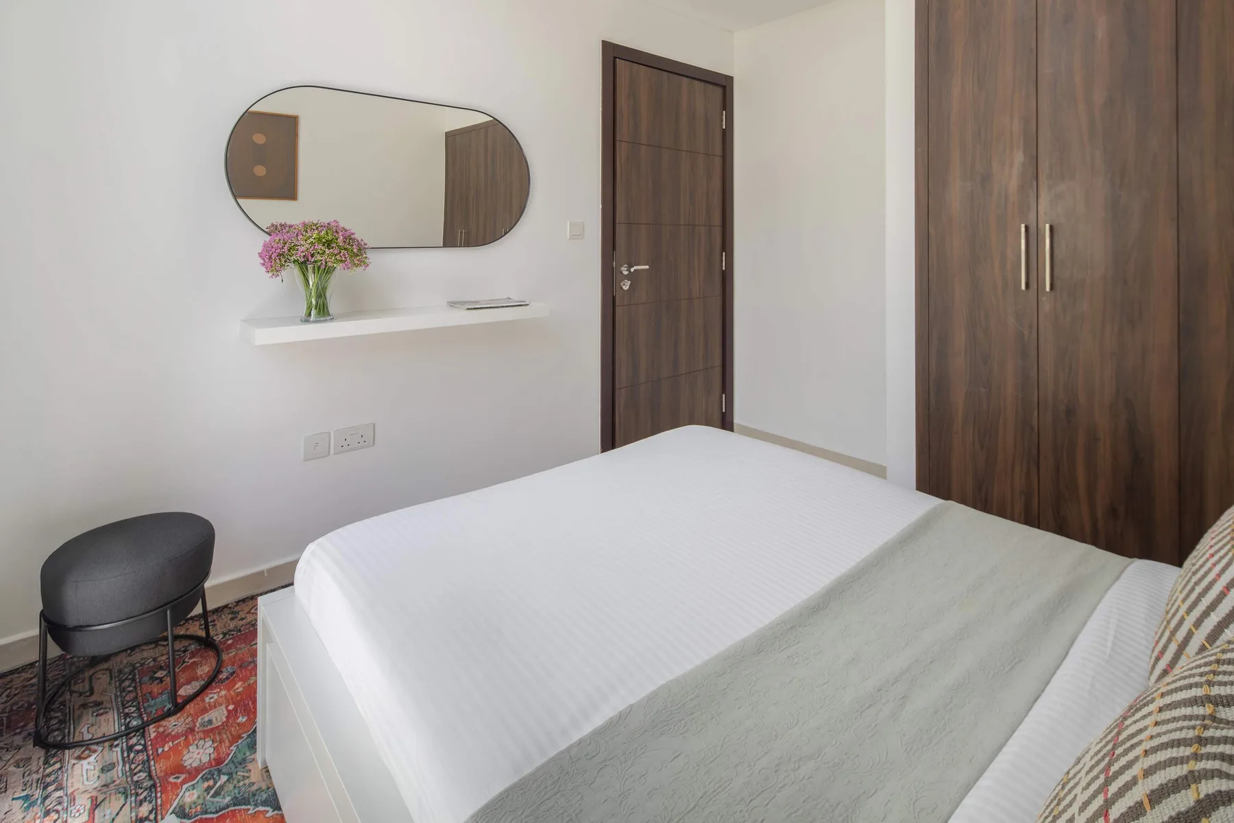 Un dormitorio con una cama bien tendida, un armario de madera oscura y un espejo de pared.