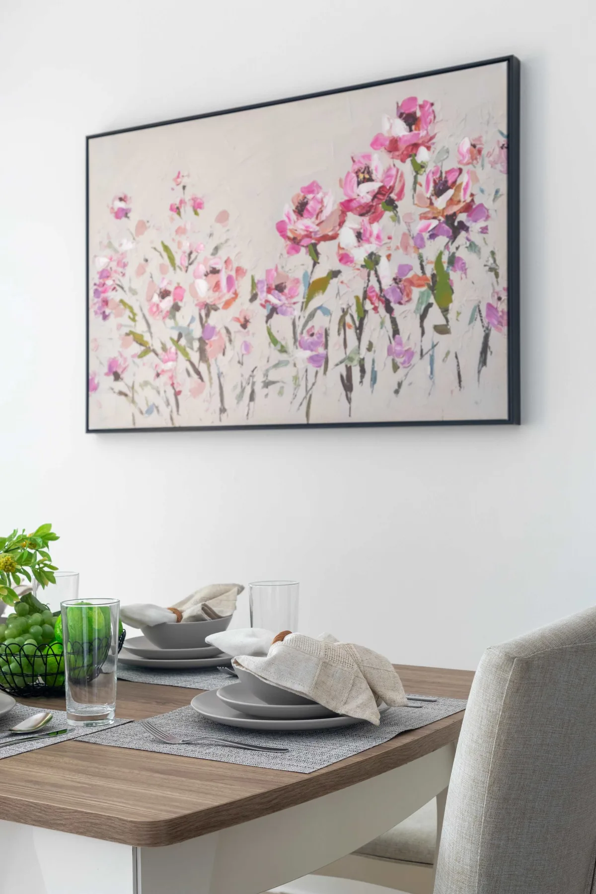 Una mesa de comedor está puesta con platos y vasos bajo una colorida pintura floral.