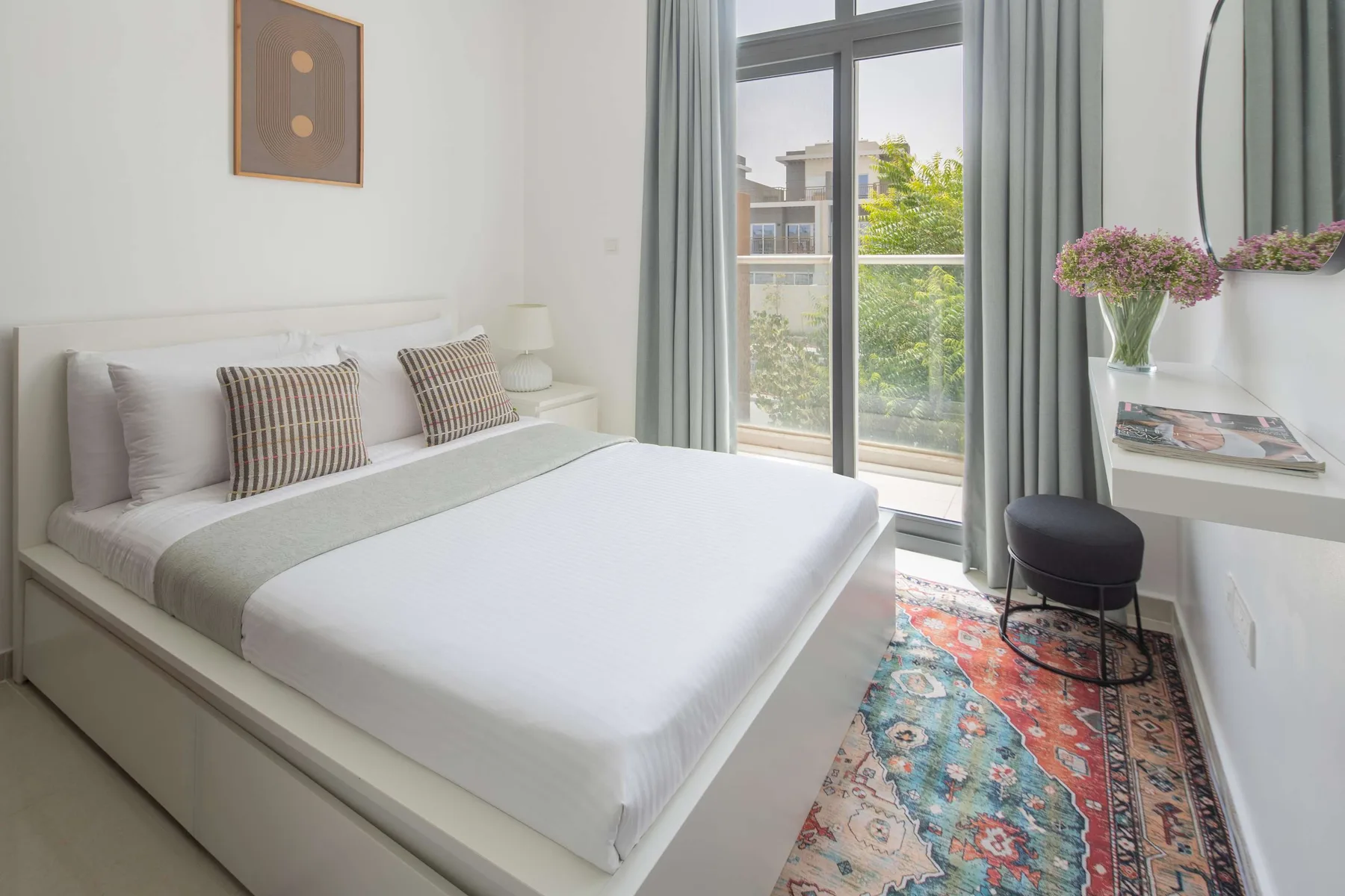Un dormitorio luminoso con una cama junto a una ventana grande y una alfombra colorida.