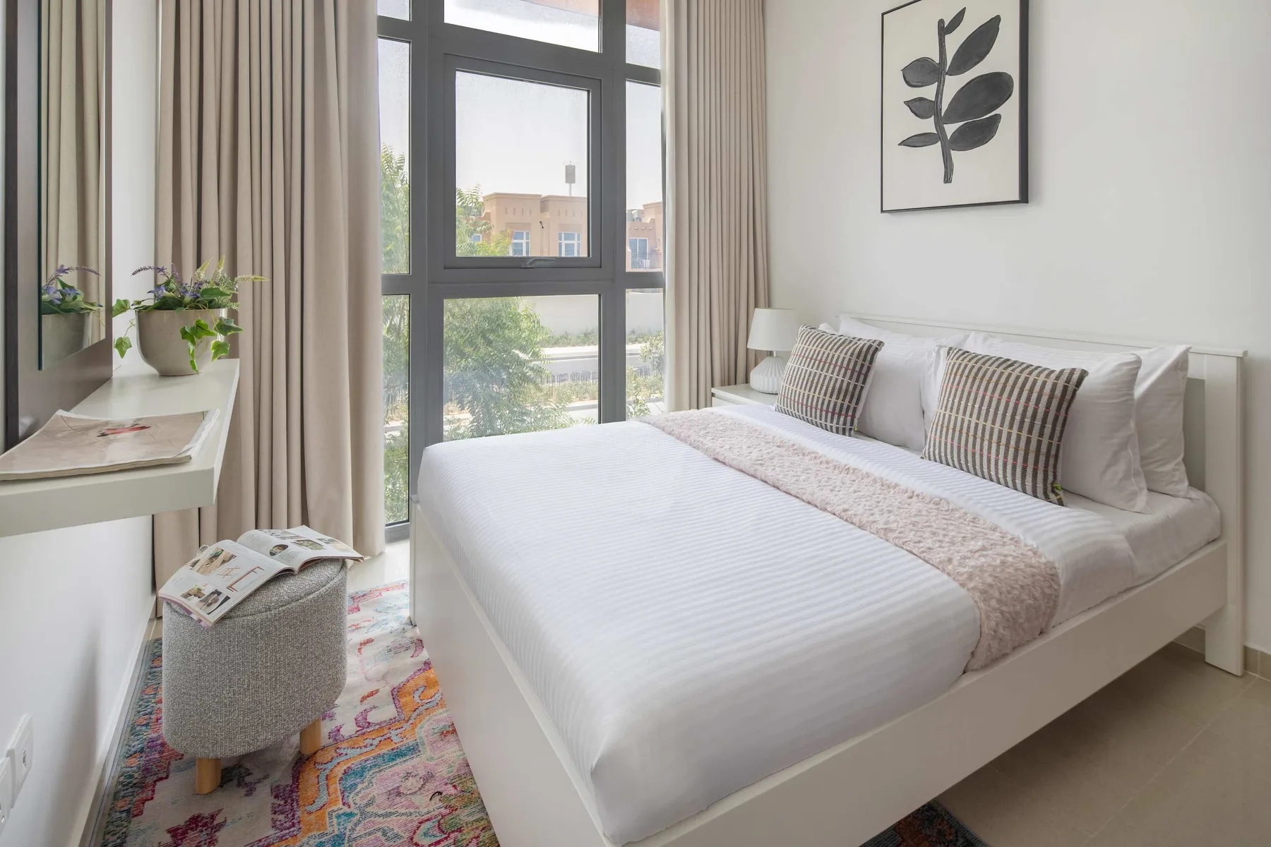 Un dormitorio luminoso con una cama bien tendida y ventanas altas.
