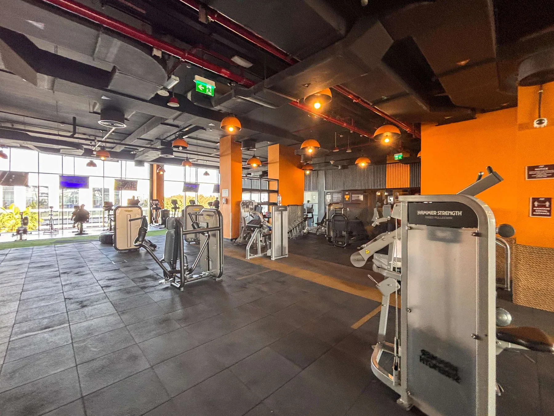 Una sala de gimnasio con máquinas de ejercicio y grandes ventanas.