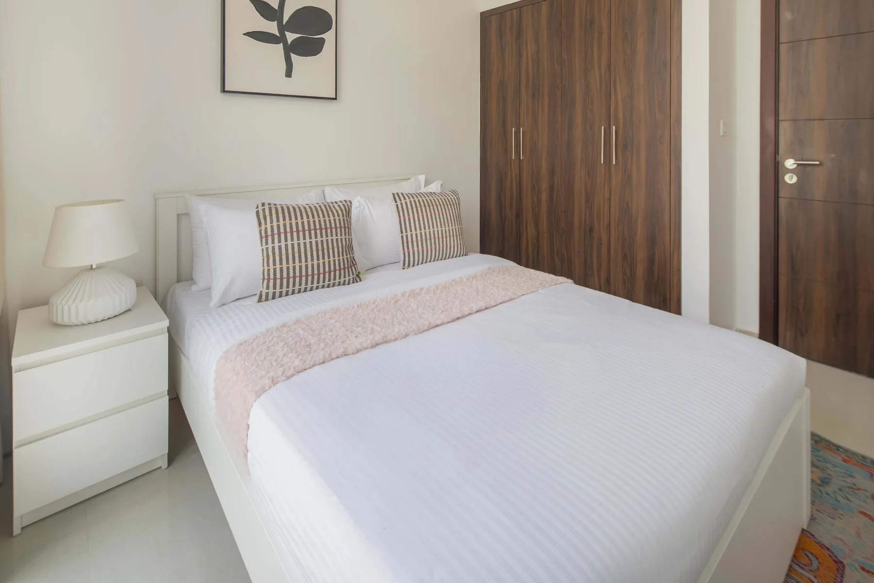 Un dormitorio con ropa de cama blanca, cojines estampados y un armario de madera.