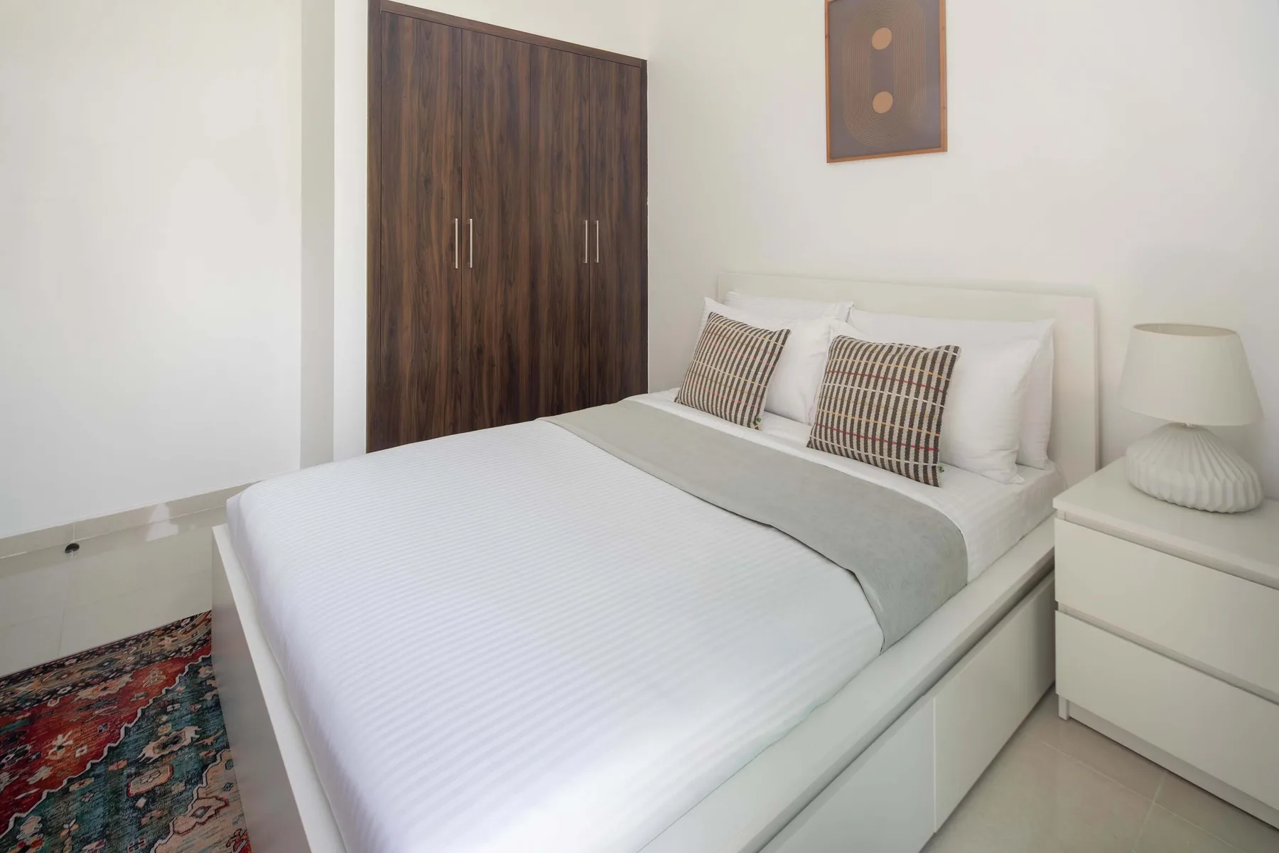 Un dormitorio luminoso con una cama bien tendida y un armario de madera oscura.