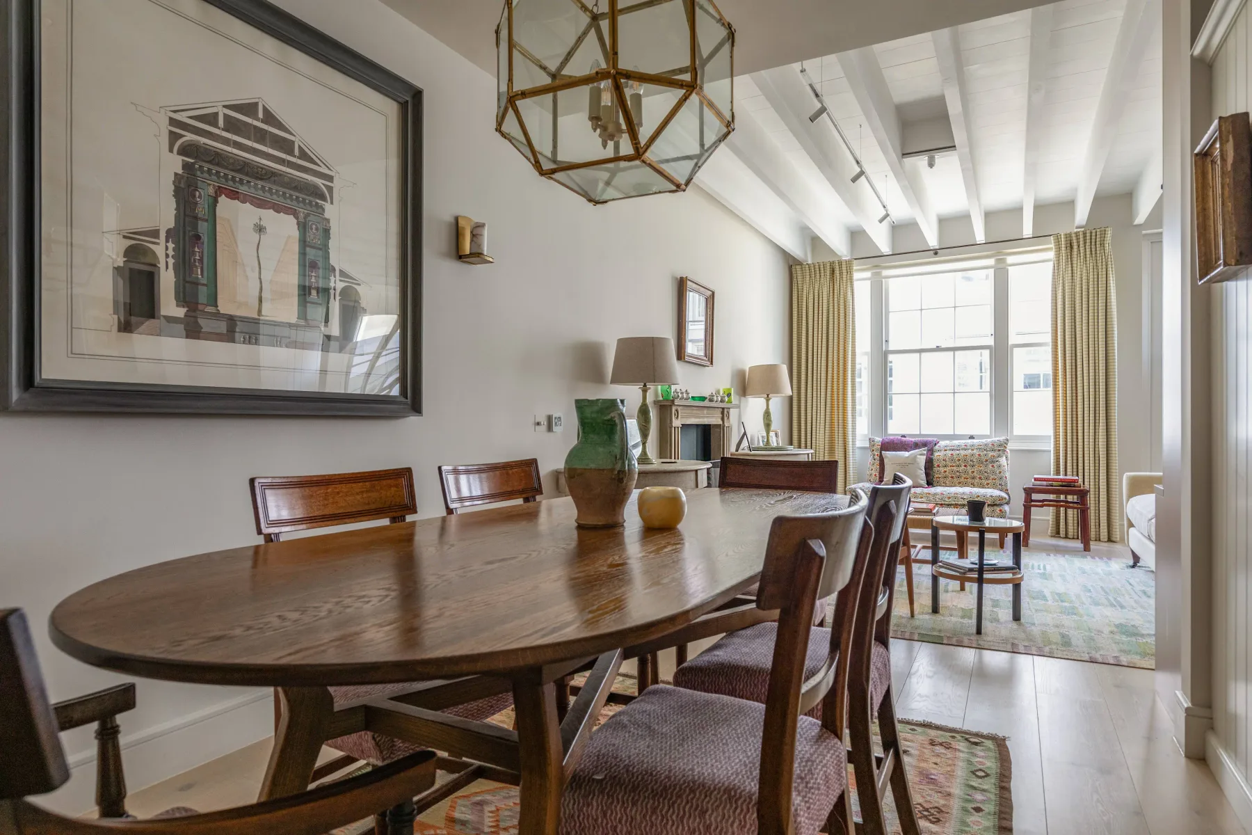 A dining area with a long wooden table and seating beside a bright living space.