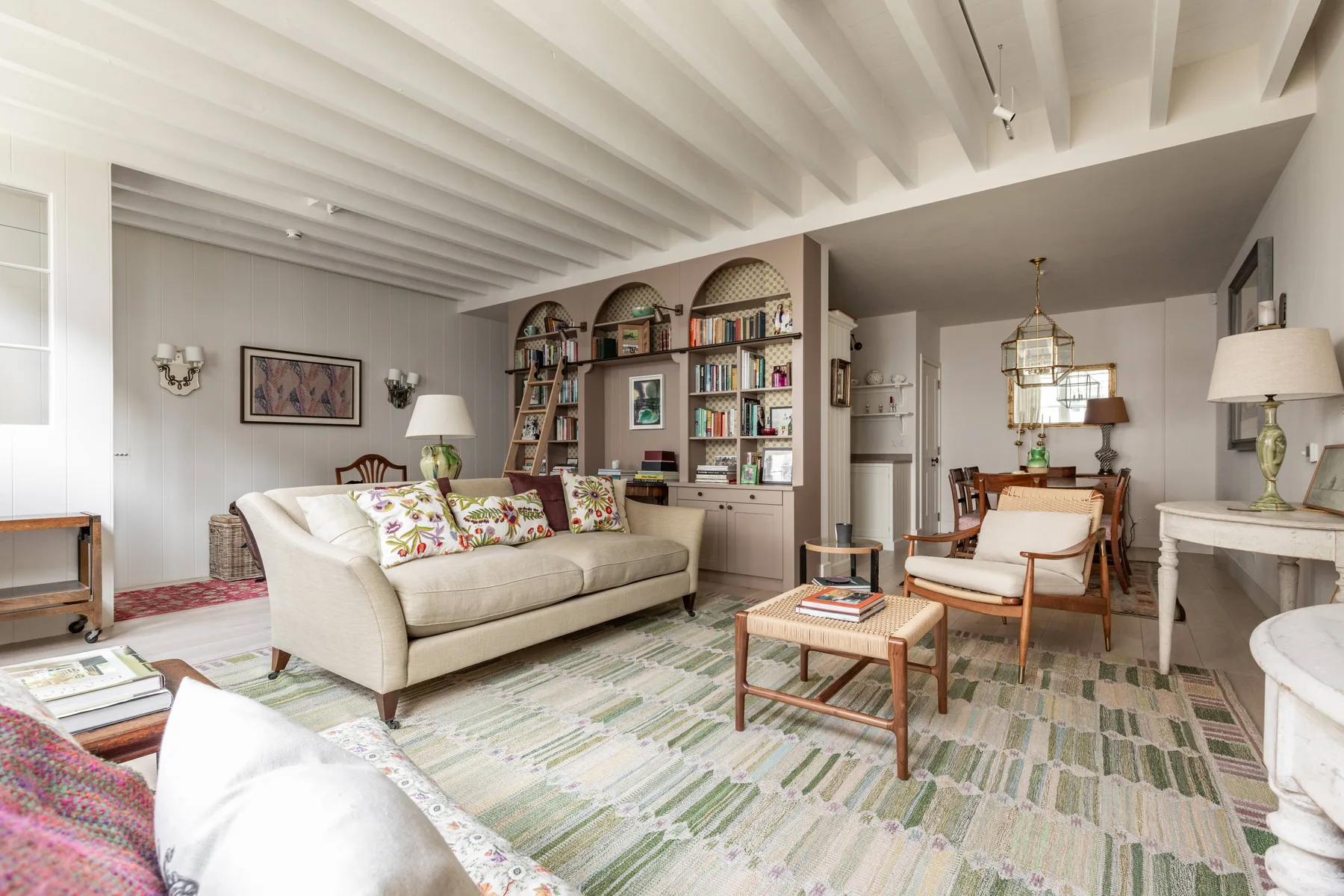A bright living room with seating, a bookshelf, and a dining area.