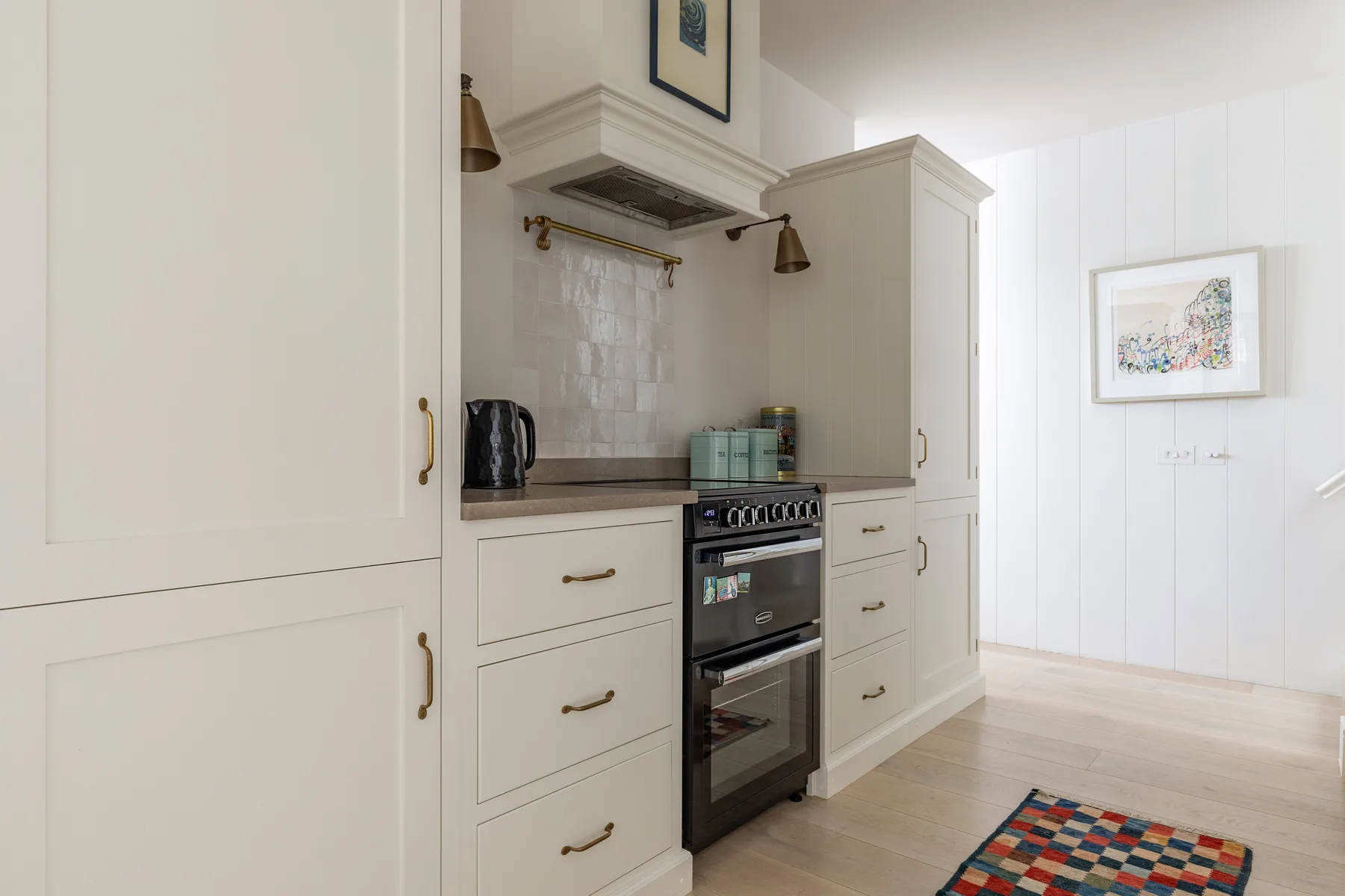 A bright kitchen with pale cabinetry, a dark range, and a colorful rug.