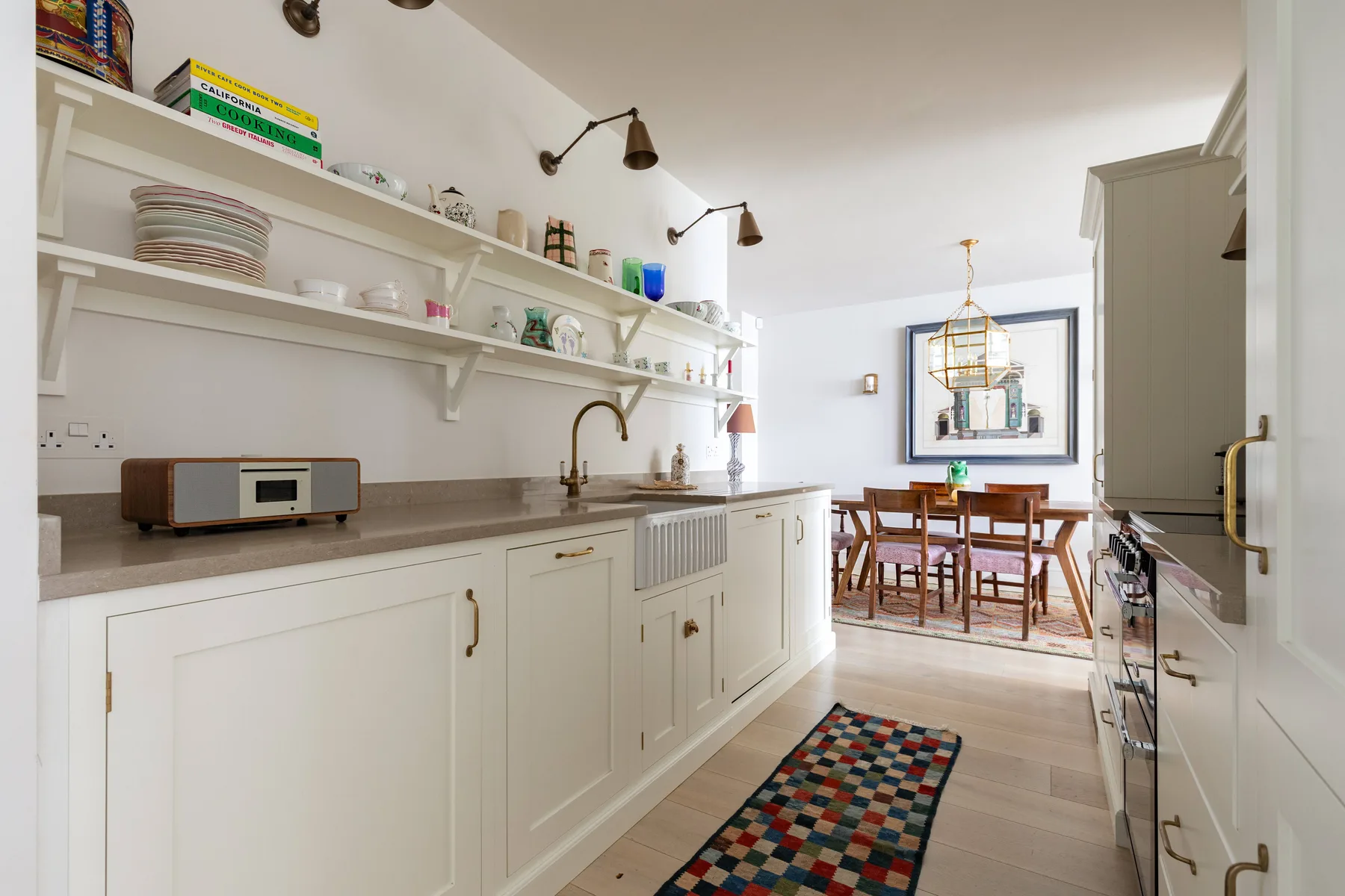 A bright kitchen with white cabinetry, open shelves, and a dining table at the far end.