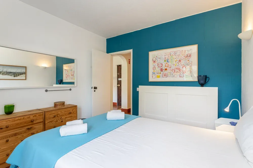 A bedroom with a white bed, turquoise bedding, and a blue accent wall.