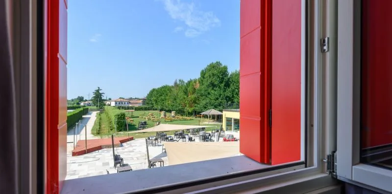An open window overlooks an outdoor seating area and green grounds.