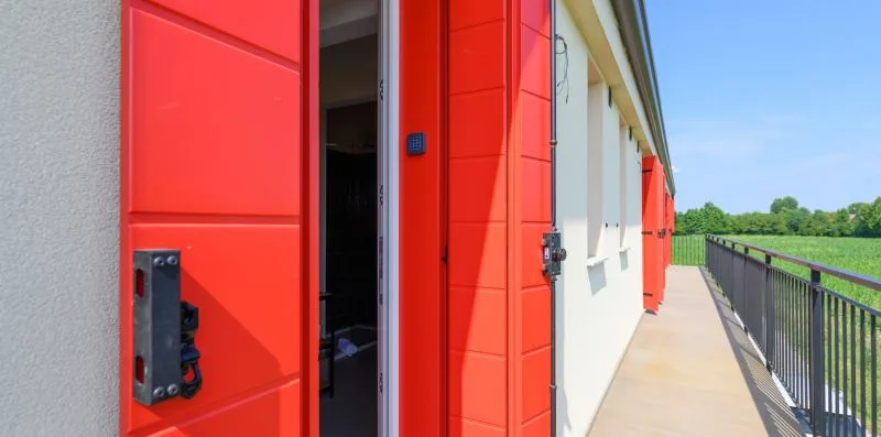 A bright red exterior door opens onto a walkway beside a railing.