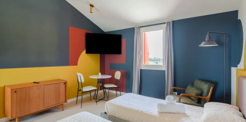 A colorful bedroom with a bed, television, and small dining table.