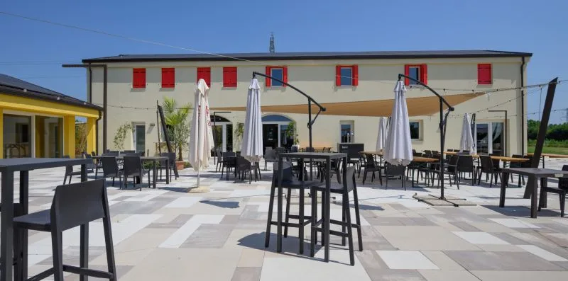 Un patio al aire libre con mesas, asientos y sombrillas cerradas frente a un edificio.