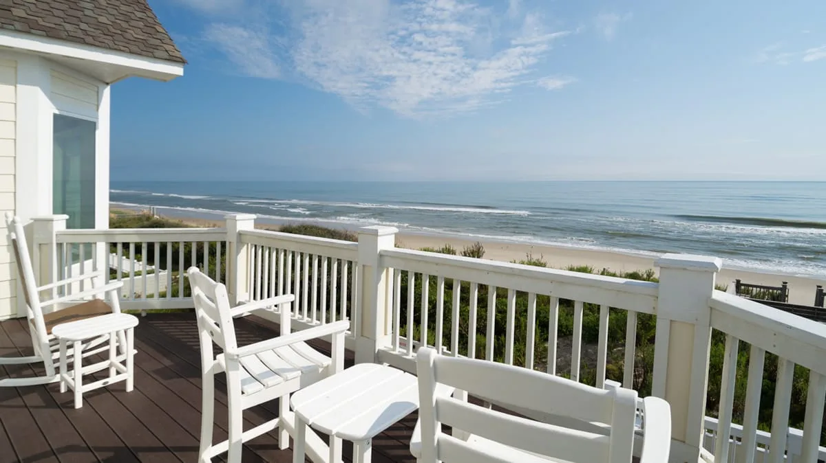 A seaside deck with white seating overlooks the ocean and shoreline.