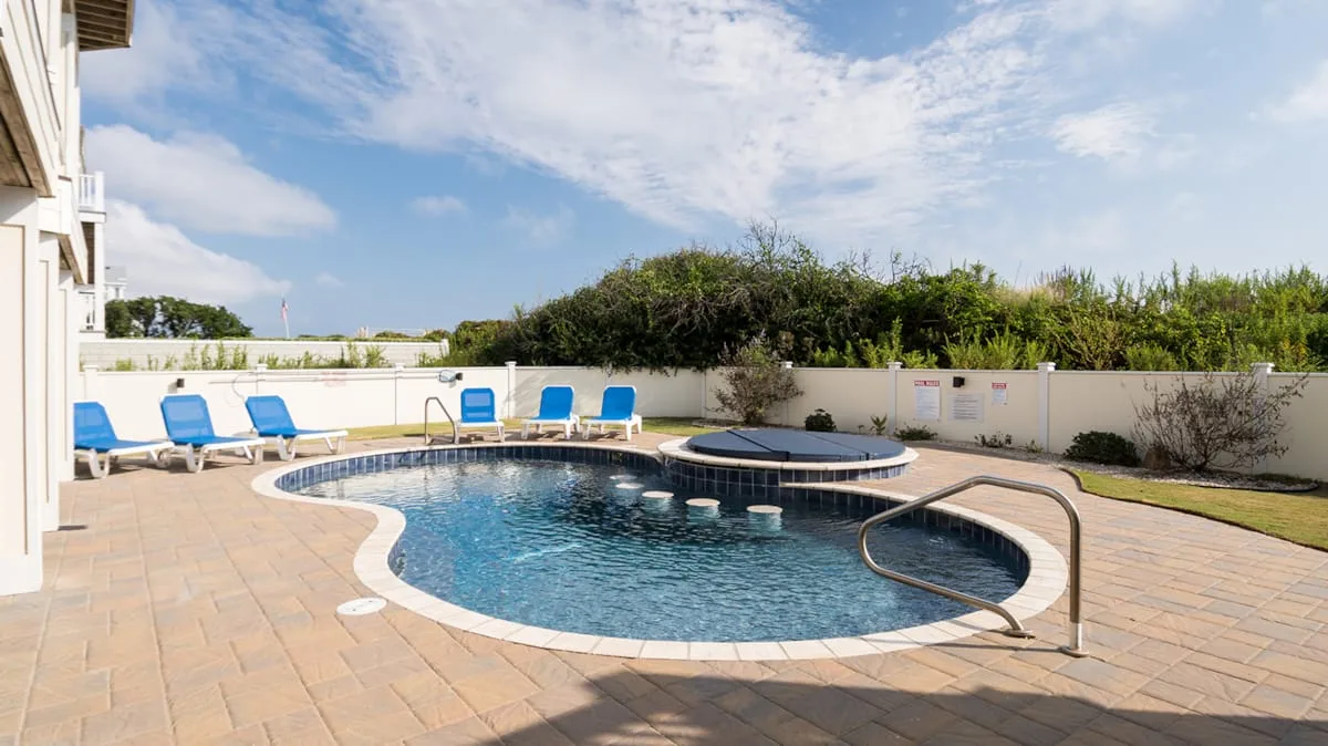 An outdoor swimming pool with a curved edge sits beside a paved patio.
