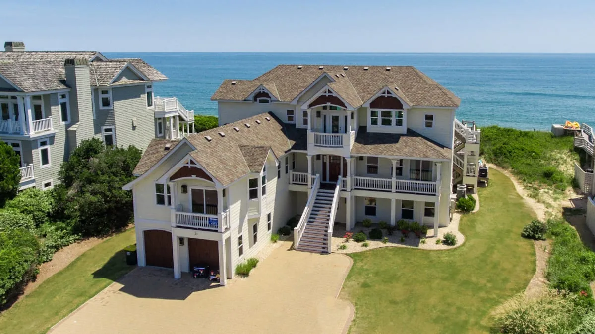 Large seaside house with balconies and a lawn beside the ocean.