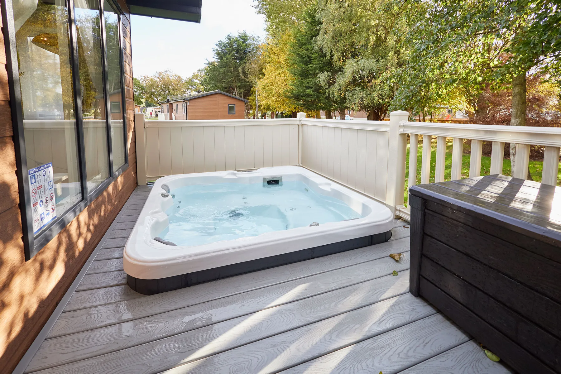 An outdoor hot tub sits on a wooden deck beside a white railing.