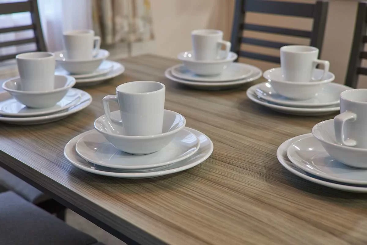 Una mesa de comedor está puesta con tazas y platos blancos.