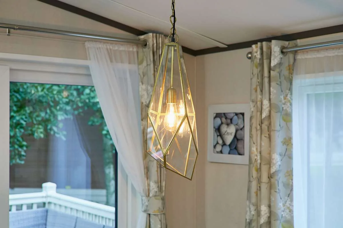 Una esquina luminosa con ventanas con cortinas y una lámpara colgante.