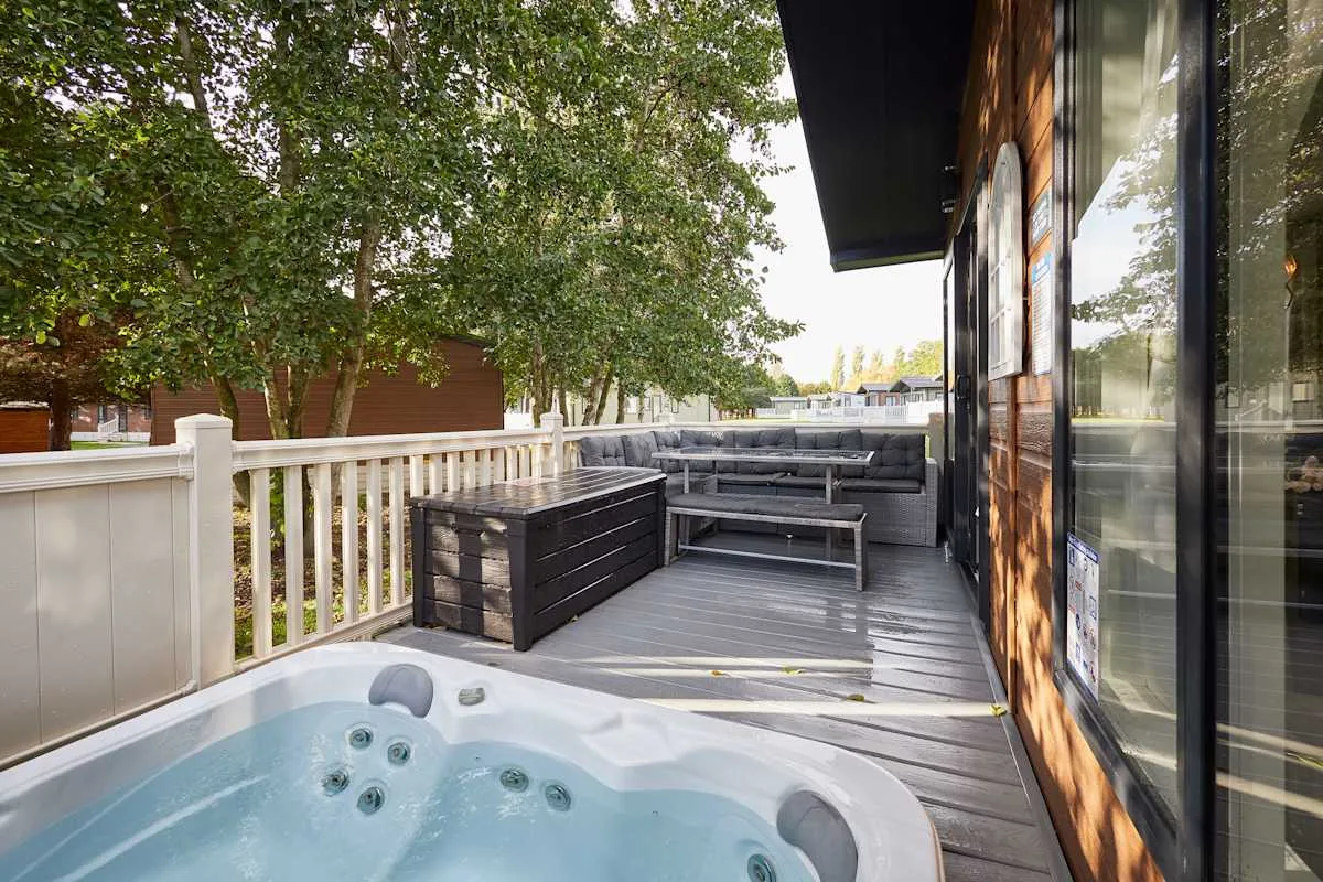 Una terraza exterior con una bañera de hidromasaje, asientos y árboles cerca.