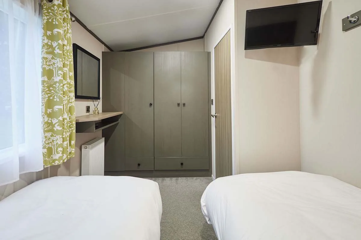 Un dormitorio con dos camas, un armario y un televisor en la pared.