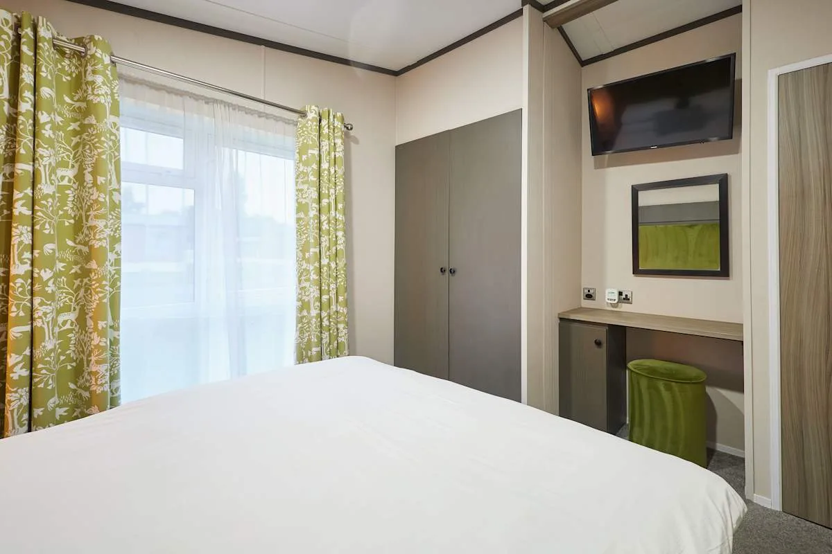 Un dormitorio con una cama grande, una ventana con cortinas y un televisor en la pared.