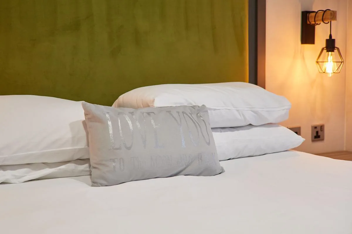 Un dormitorio con ropa de cama blanca y un cojín decorativo.