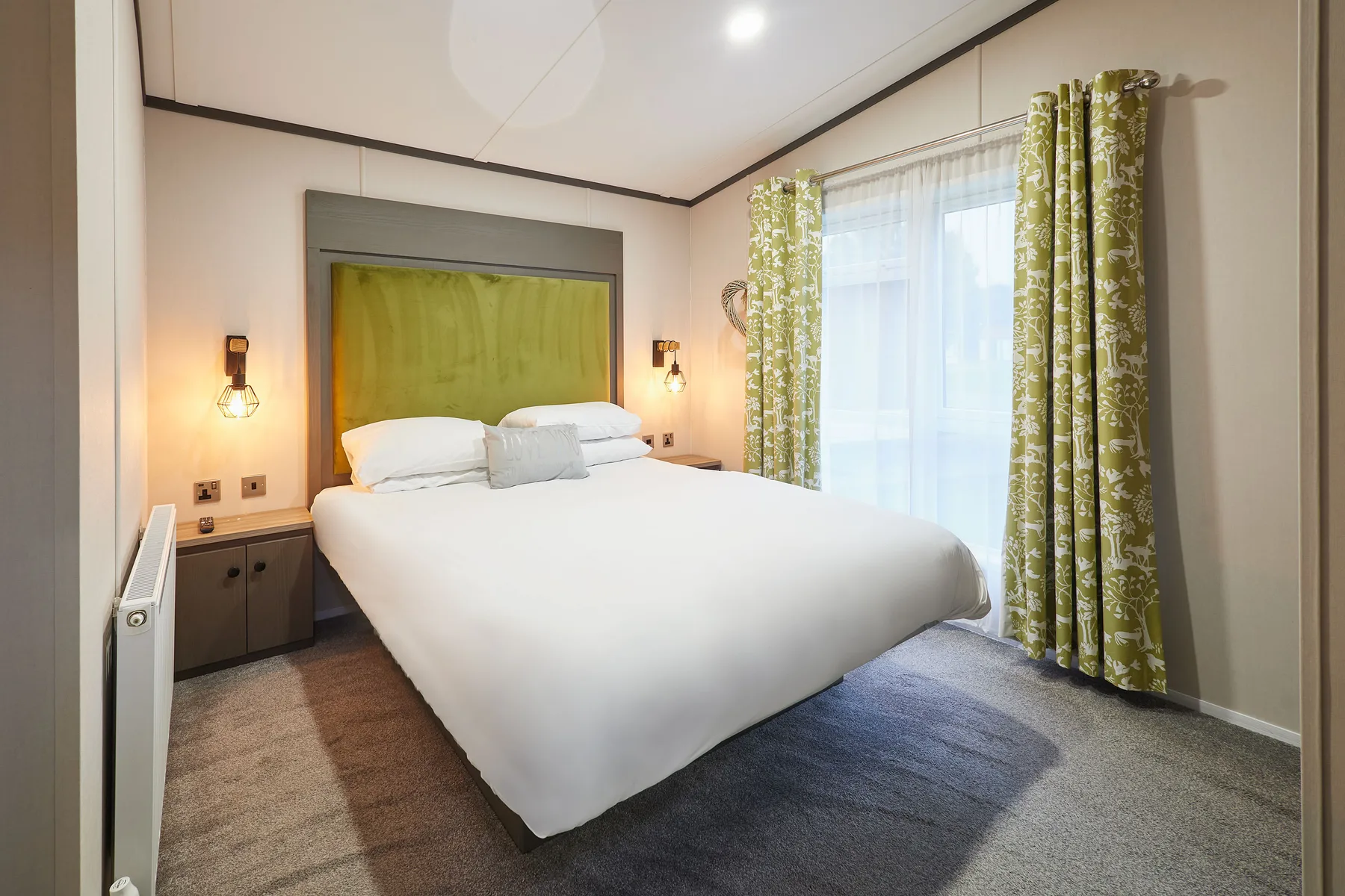 Un dormitorio con una cama bien hecha y cortinas estampadas junto a una ventana luminosa.
