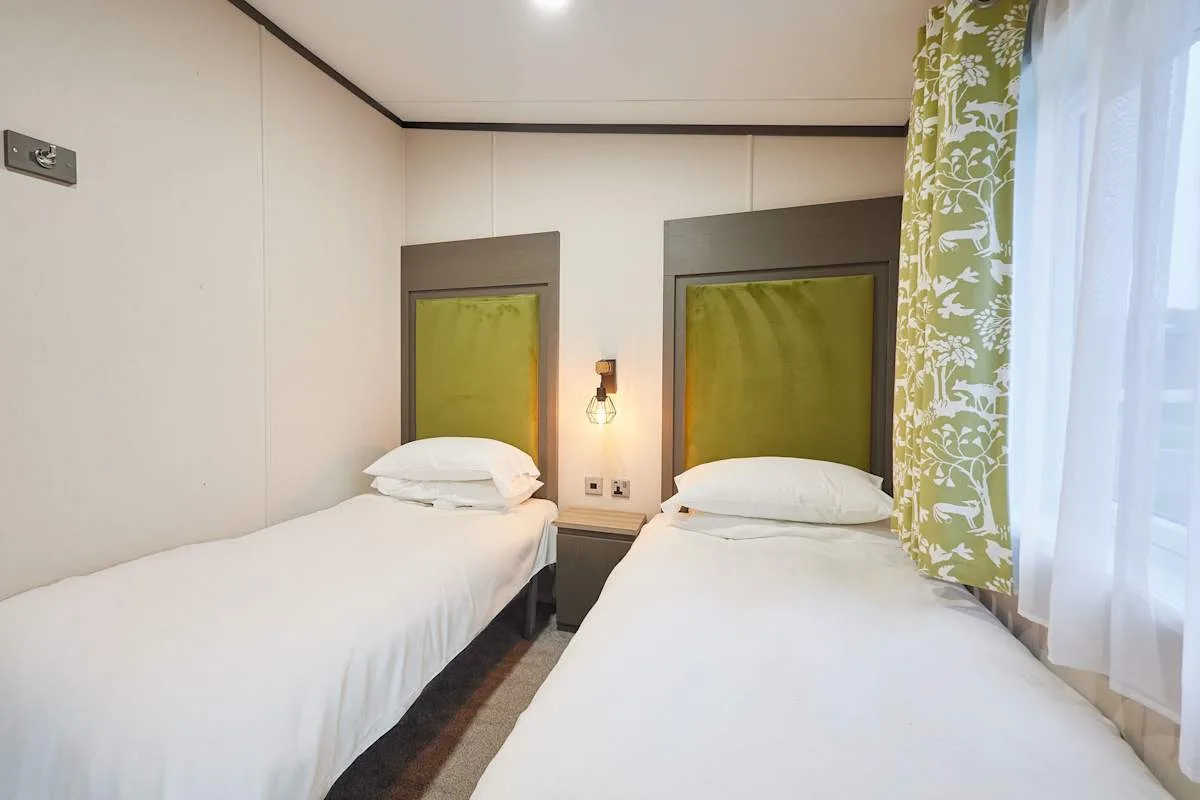 Un dormitorio con dos camas individuales y una ventana con cortinas verdes.