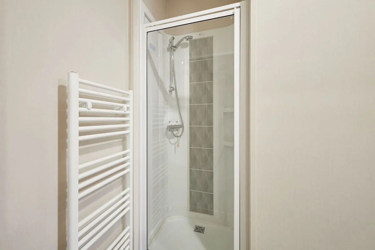 Una ducha de baño con un toallero térmico blanco al lado.