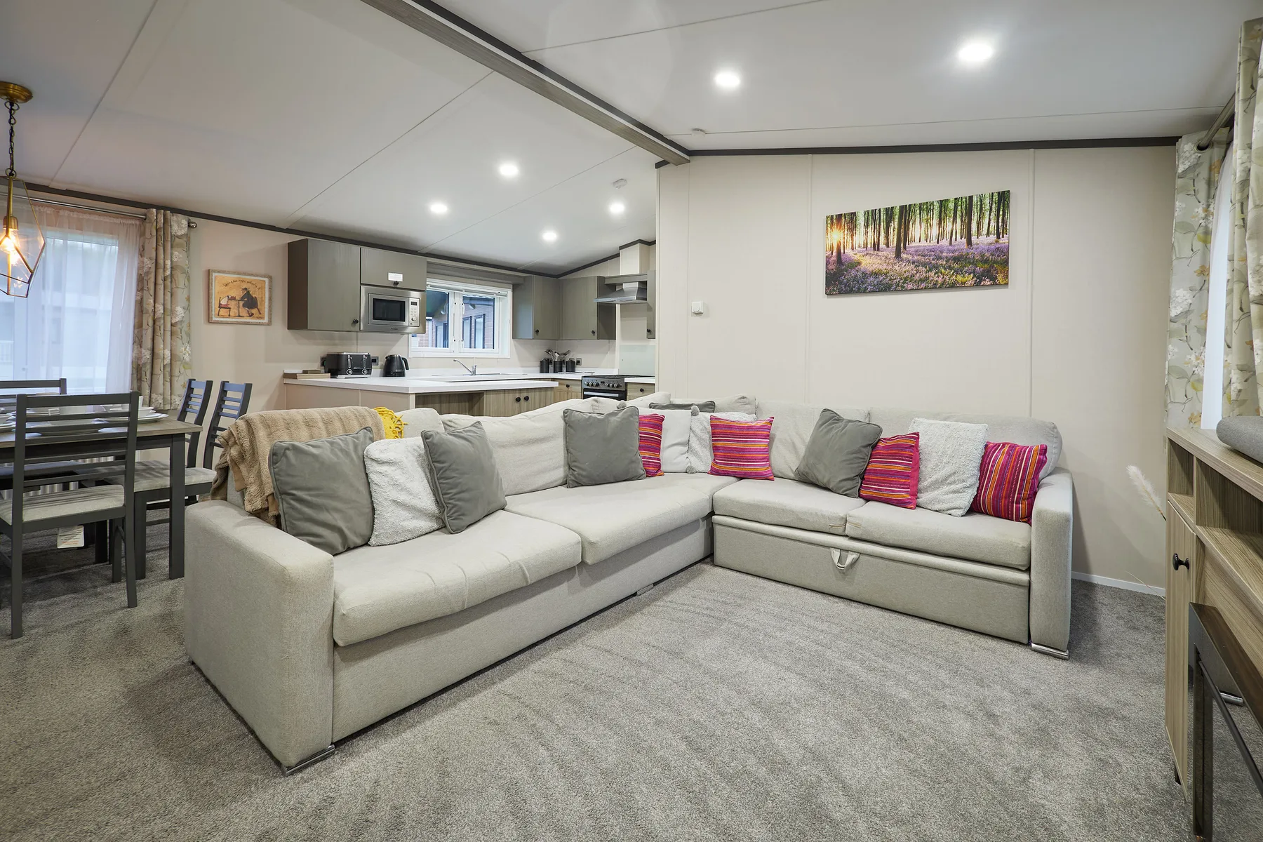 A bright living room with a sectional sofa and an open kitchen behind it.