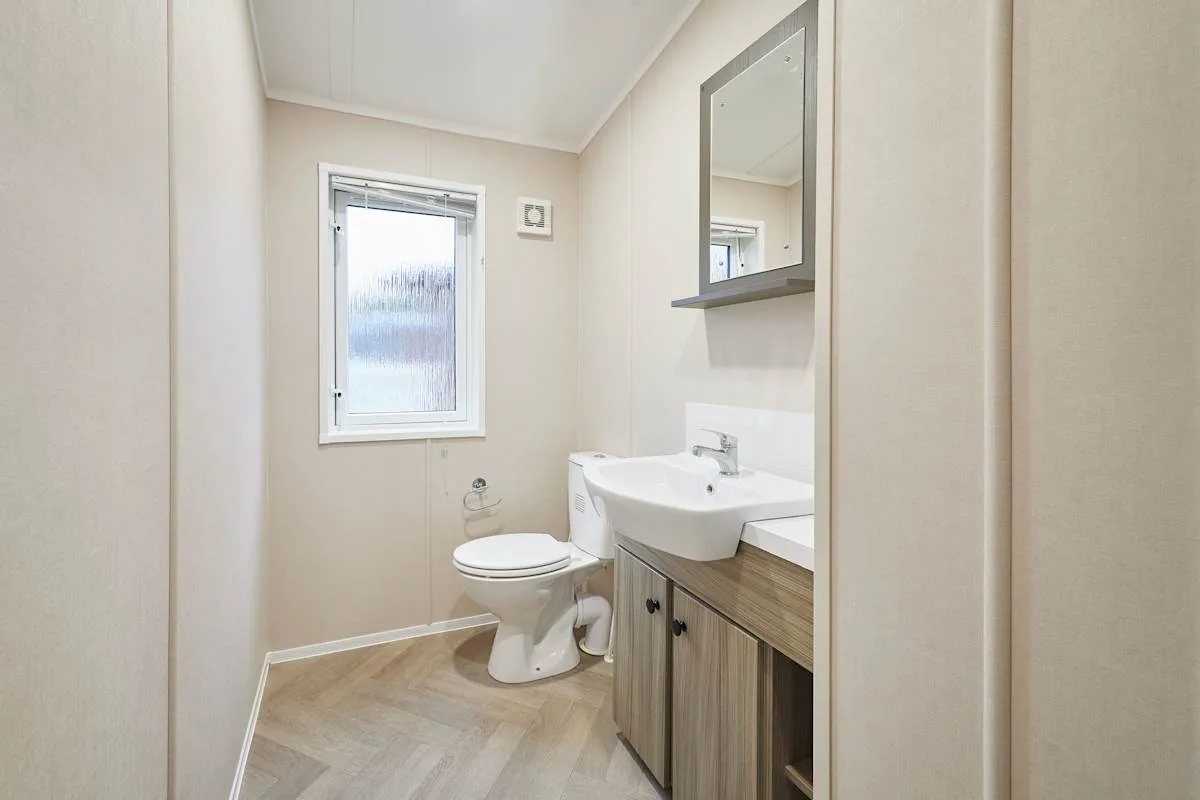 Un baño con inodoro, lavabo y ventana esmerilada.