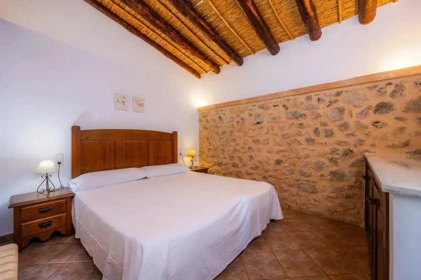 A bedroom with a bed beneath a wooden-beam ceiling and a stone wall.