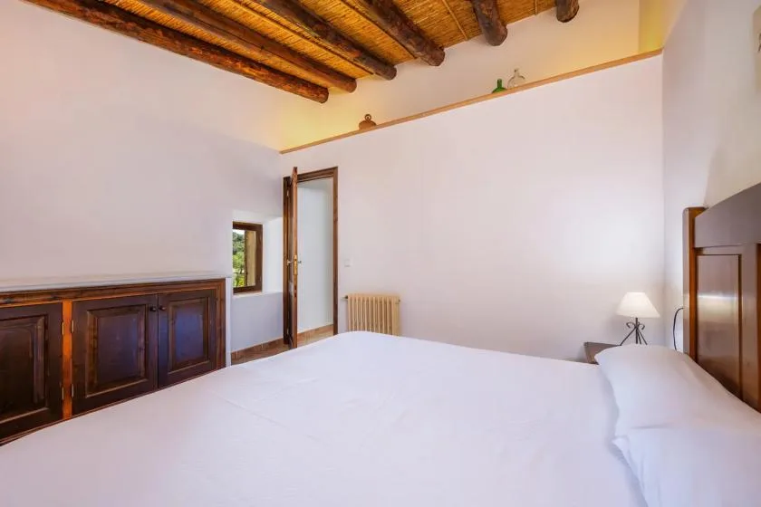 A bedroom with a large bed, dark wooden cabinet, and exposed ceiling beams.